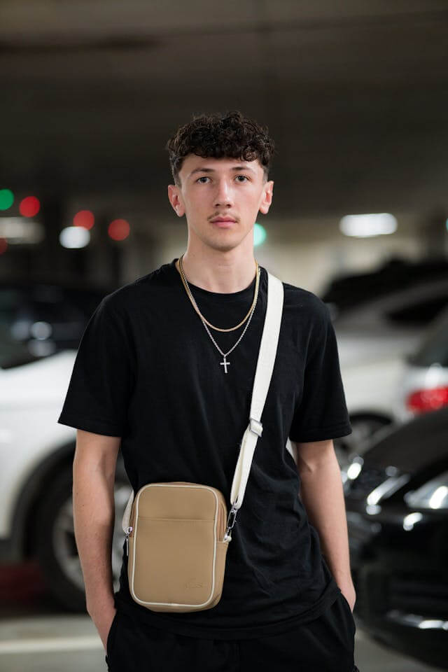Homem jovem usando camiseta preta e uma bolsa com a alça transversal sobre o peito.