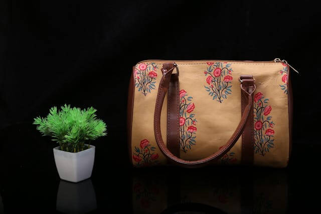 bolsa com bordado de flores sendo exposta ao lado de um vaso pequeno de plantas